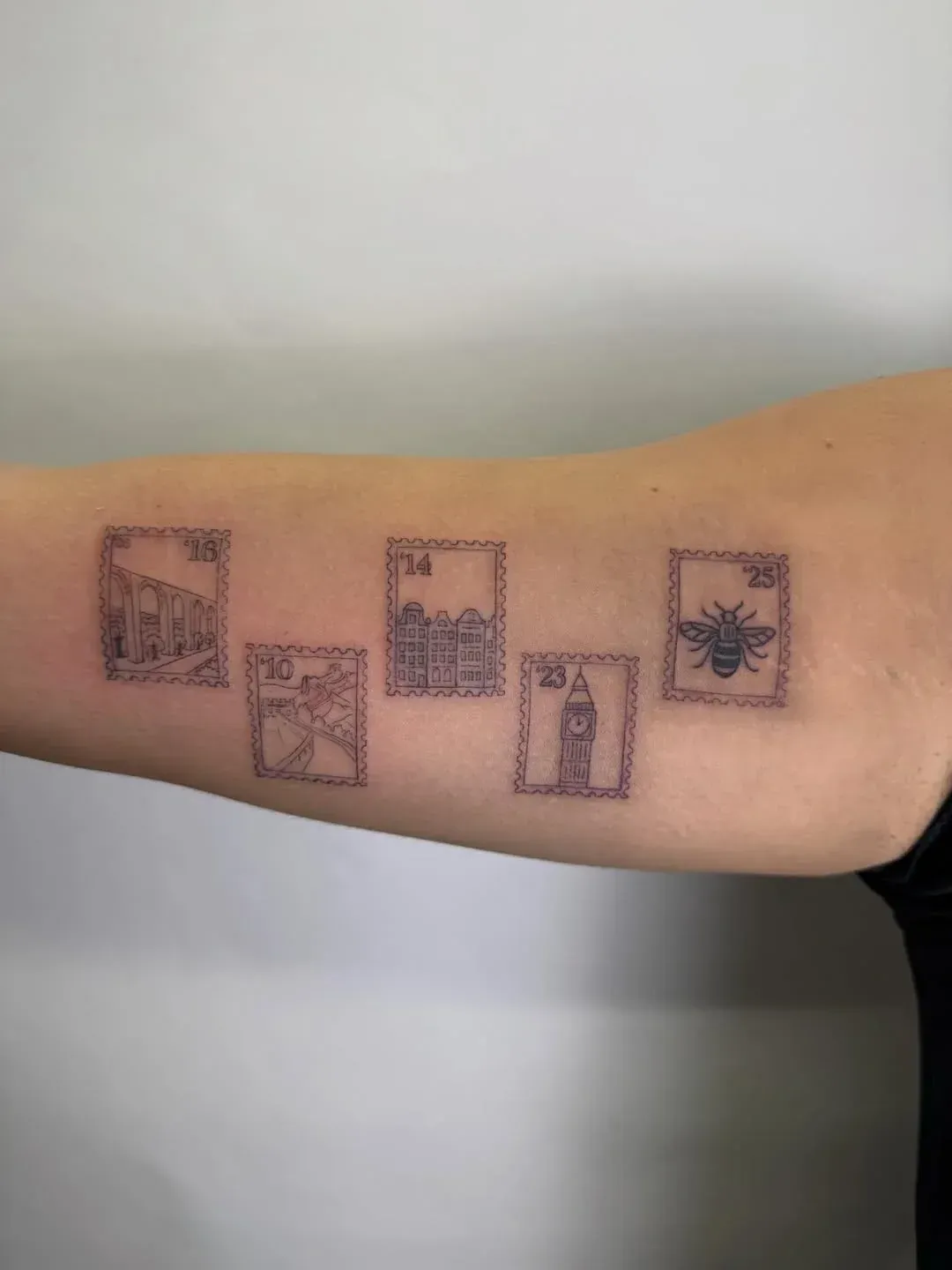 A forearm tattoo featuring five rectangular postage stamp designs depicting landmarks and a bee, done in fine-line black ink.