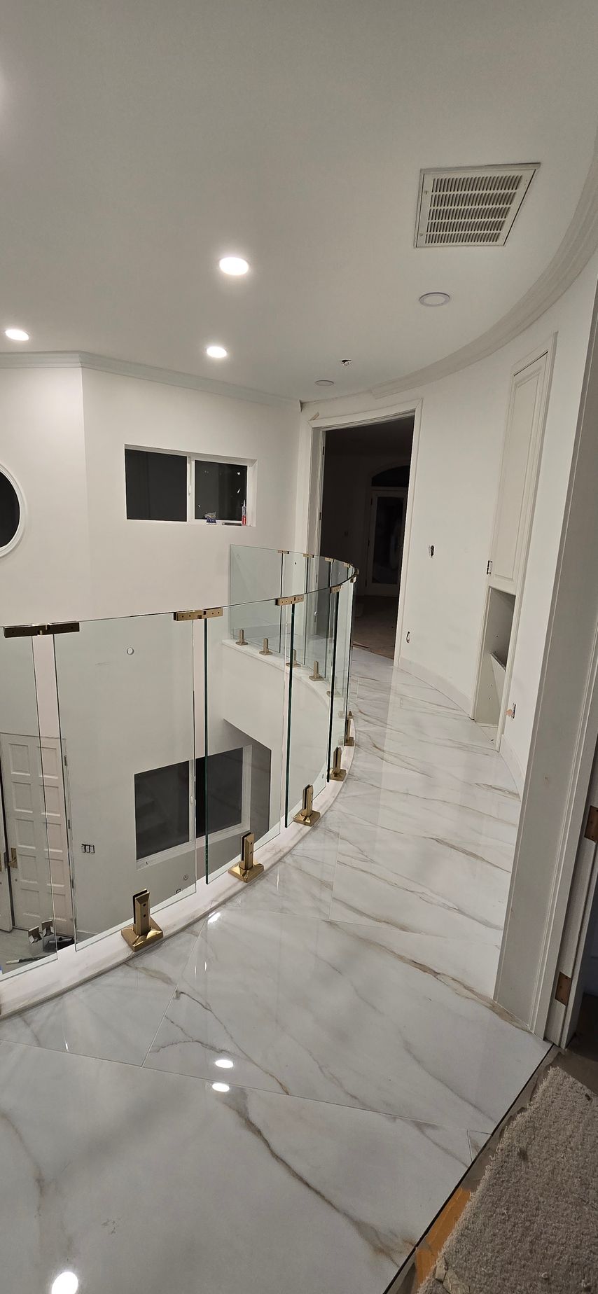 Interior hallway with white walls and marble floors, glass railing.