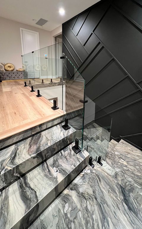 Staircase with marble steps, glass railing, and black paneling. Wooden flooring on landing.