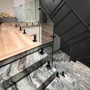 Staircase with marble steps and glass railing, black metal supports, wooden floor, and dark gray wall.