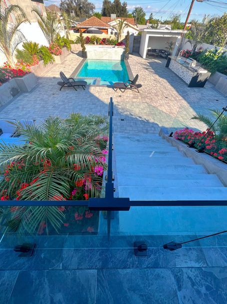 Looking down concrete steps towards a pool, patio, and outdoor kitchen.