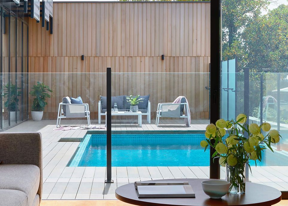 Poolside seating area viewed from inside the house with a pool, deck, and plants.