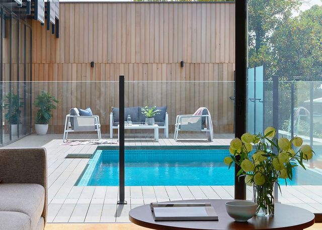 A small outdoor pool with lounge seating, wooden deck, and glass fence.