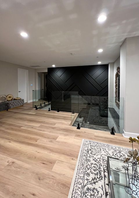 Modern interior with wooden floors, black accent wall, glass railing, and staircase.