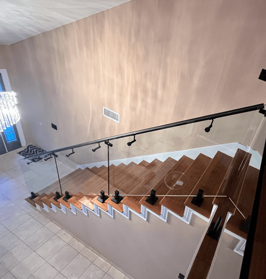 Staircase with wooden steps, glass panel railing, and black handrail. Light colored walls and tile flooring.