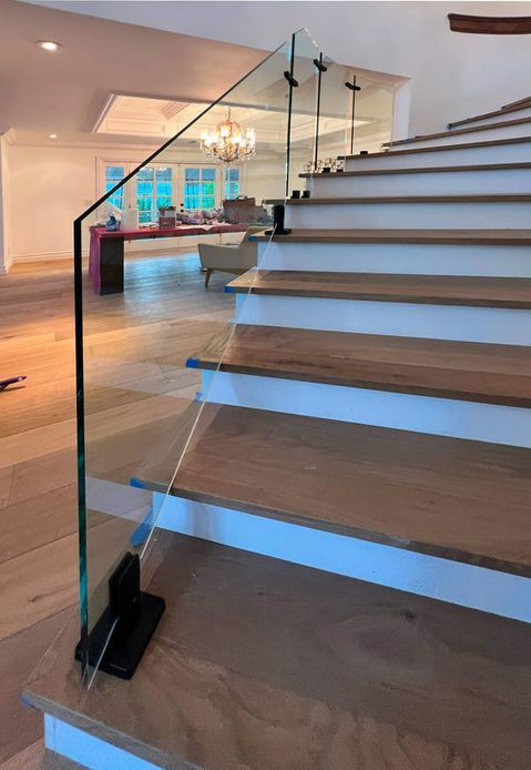 Staircase with wooden steps and glass railing, viewed from below.