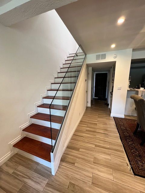 Staircase with wooden steps and glass railing in a brightly lit entryway, leading upwards.