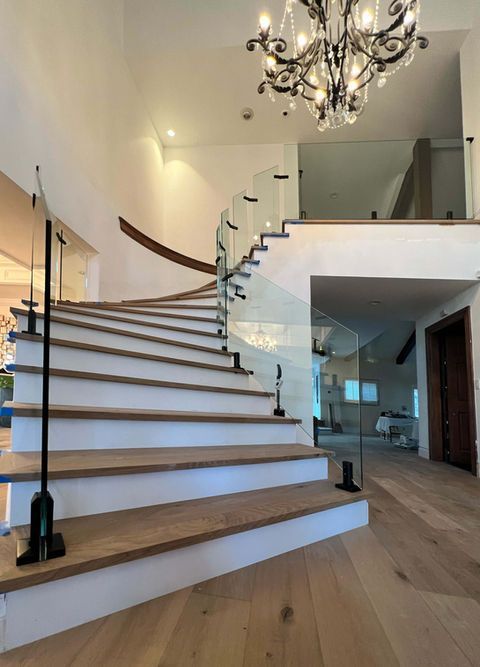 Modern staircase with glass railing and chandelier in a bright interior.