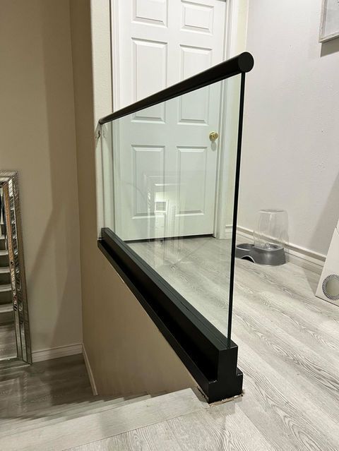 Glass railing with black frame beside a staircase, leading to a door.