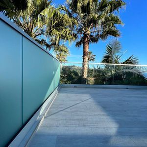 Balcony with frosted blue glass panels and palm trees under a blue sky.