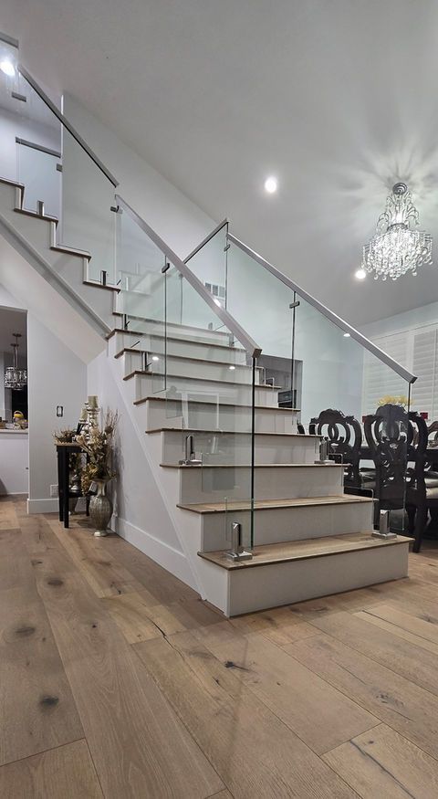 Staircase with glass railing, light wood floors, and white walls in a modern home interior.