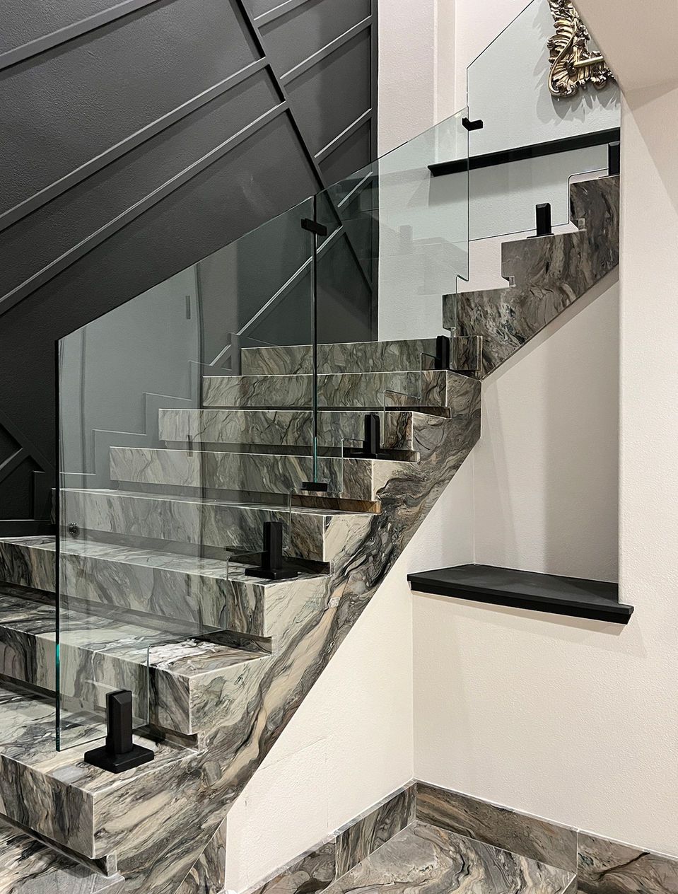 Marble staircase with glass railing, black metal supports, and neutral-colored walls.