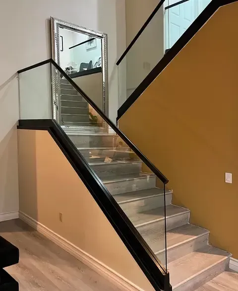 Staircase with glass and black railings, light-colored walls, and a large mirror reflecting the stairs.
