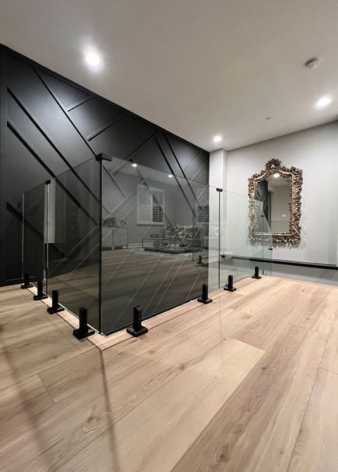 Glass railing with black posts against a dark diagonal-paneled wall, light wood floor, and ornate mirror.