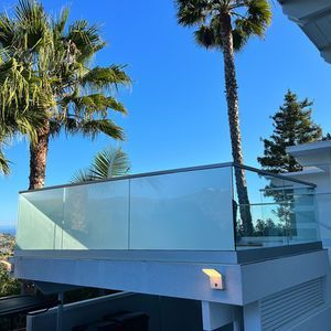 Glass balcony with palm trees against a clear blue sky.