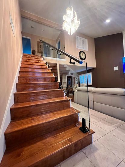 Wooden staircase with glass railing. High ceiling, chandelier. Bright, modern interior.