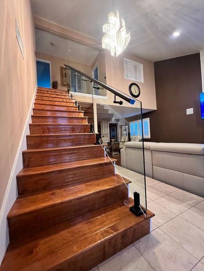 Wooden staircase leads to upper level with glass railing and chandelier.