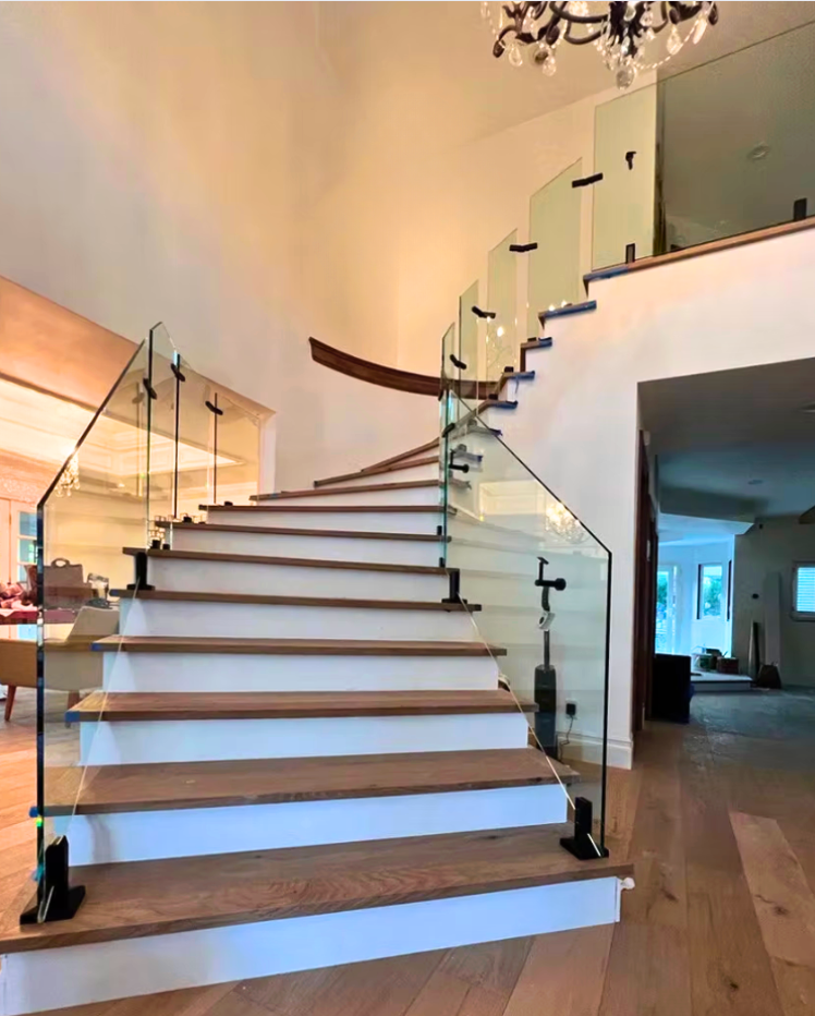 Staircase with wooden steps and glass railing, in a modern, well-lit home.