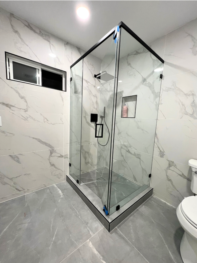 Modern bathroom with glass shower enclosure, marble tile walls, and gray flooring.