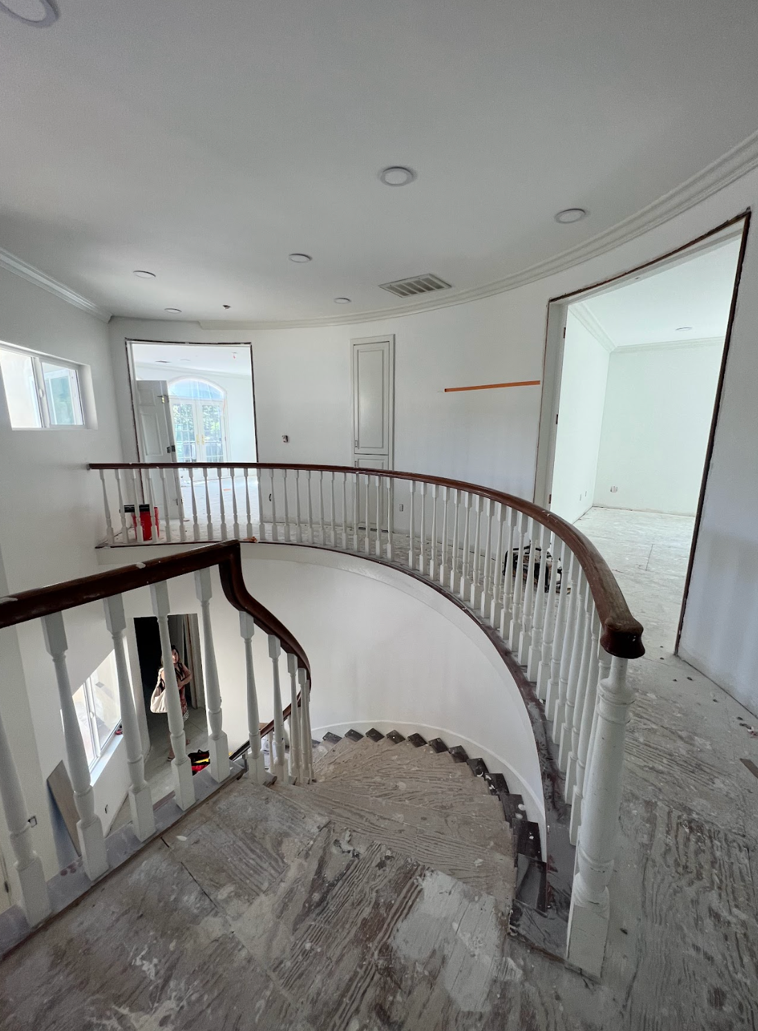 Interior view of a curved staircase with white walls, brown banister, and an open doorway.