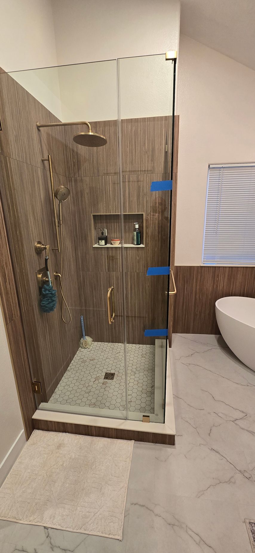 A modern bathroom with a glass-enclosed shower featuring brown tiled walls and a white marble floor.