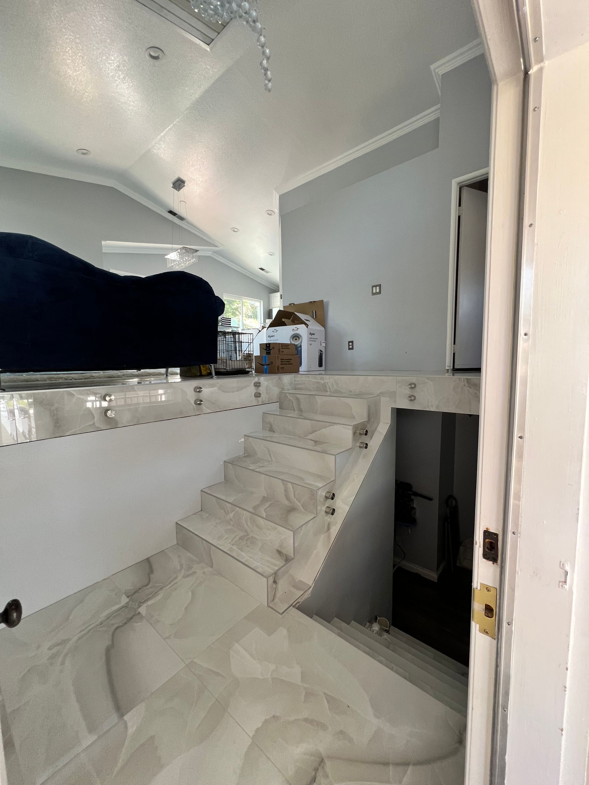 Interior view of a modern home with a staircase, raised platform, and white and gray tiling.