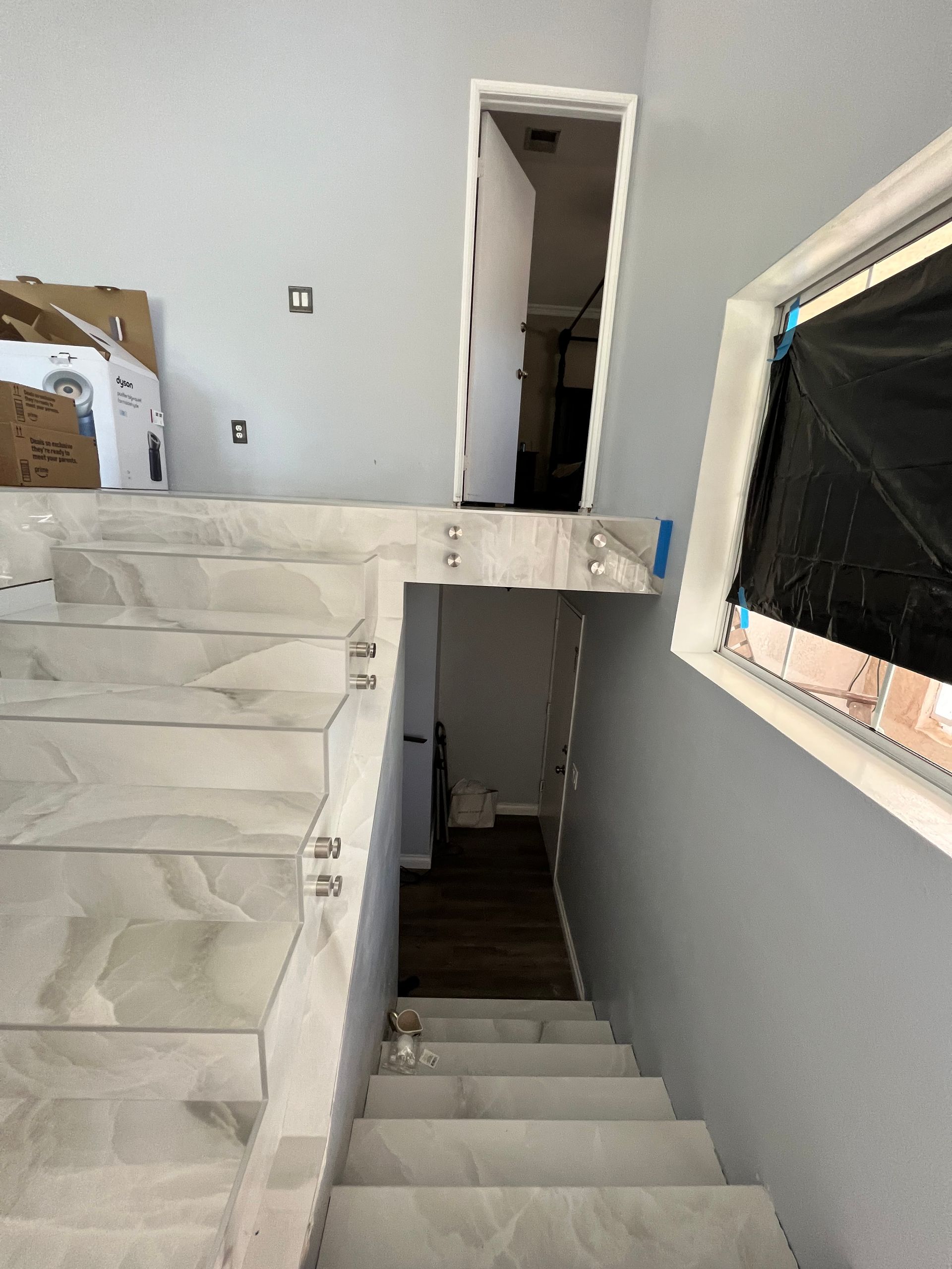 Staircase with tile steps leads down to a doorway. Light grey walls and a window with plastic covering.