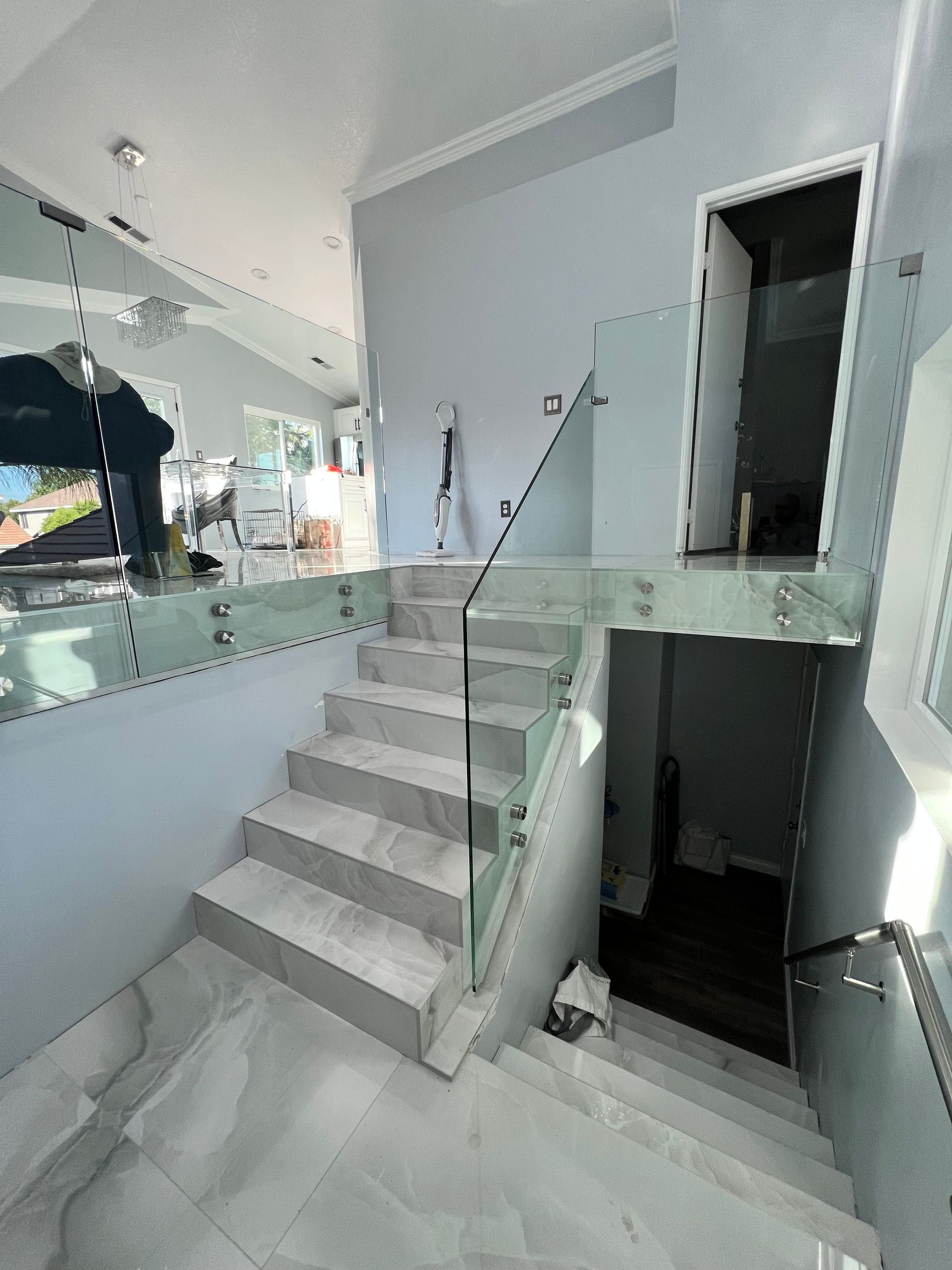 Staircase with glass railing, gray marble steps, and mirrored wall in a modern home.