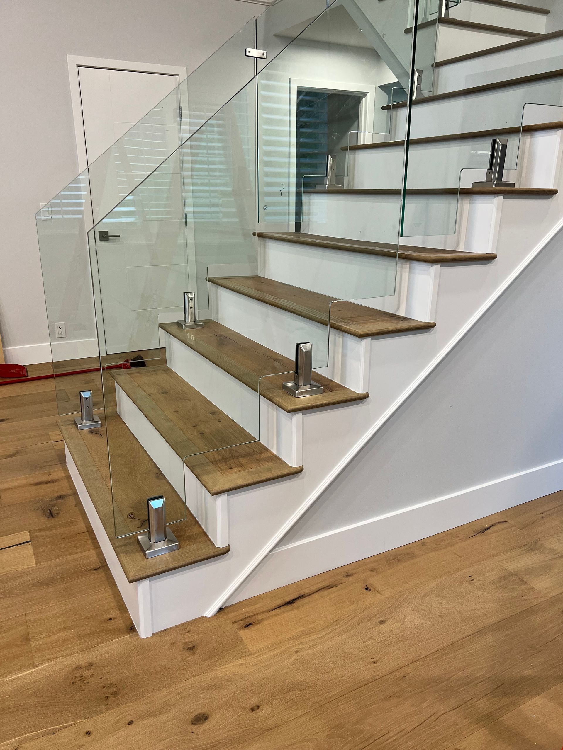 Staircase with wooden steps and glass railing, stainless steel posts. The walls are white with wooden flooring.