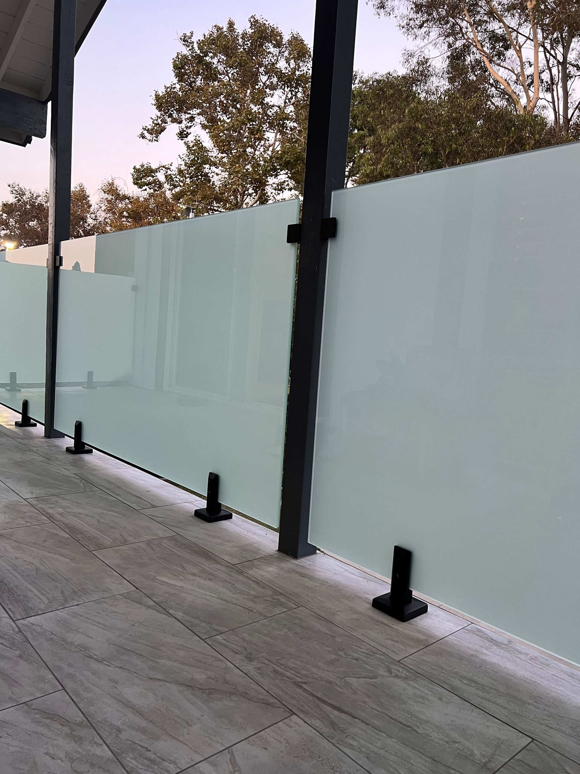 Frosted glass panel railing on a patio, attached to black square posts.