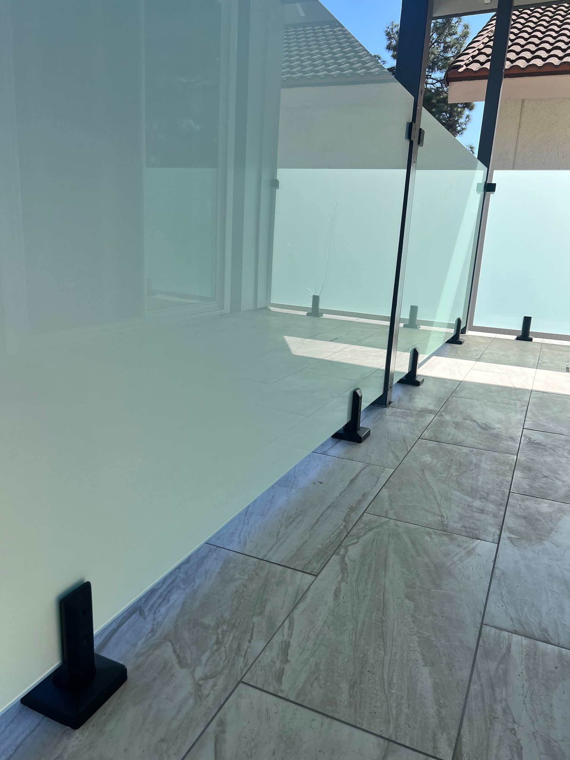 Glass panel railing on a tiled patio. Black brackets hold the clear panels in place.