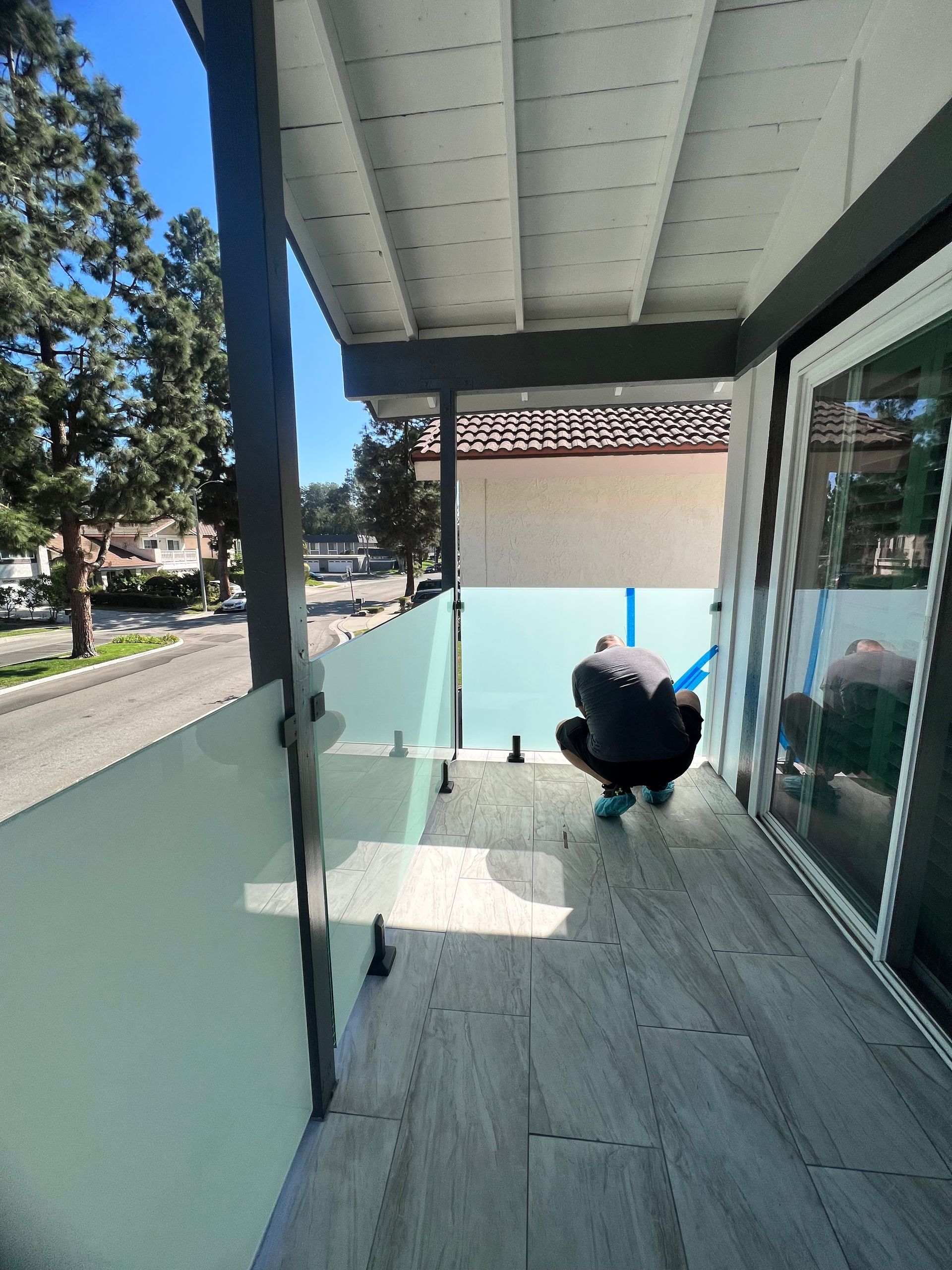 Person installing glass panels on a balcony with a view of a street and houses.
