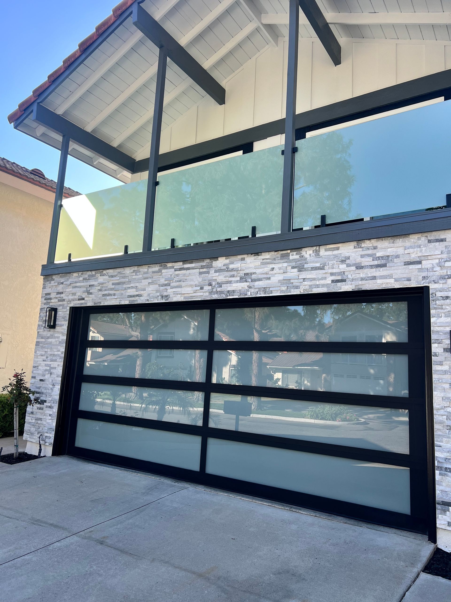 Modern garage with glass door and frosted glass balcony railing, white stone facade.