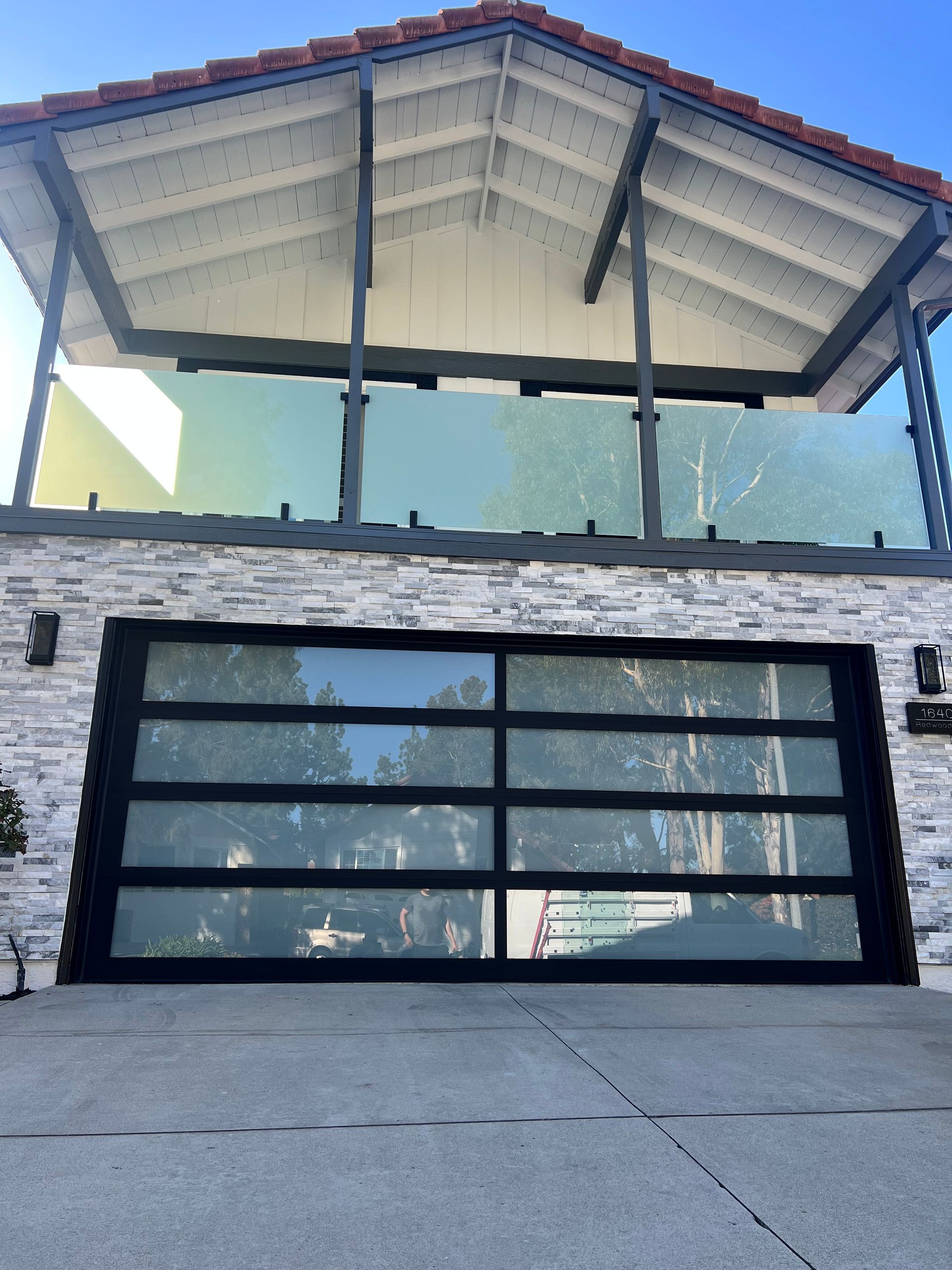 Modern house with glass garage door and balcony, gray stone facade, blue sky.
