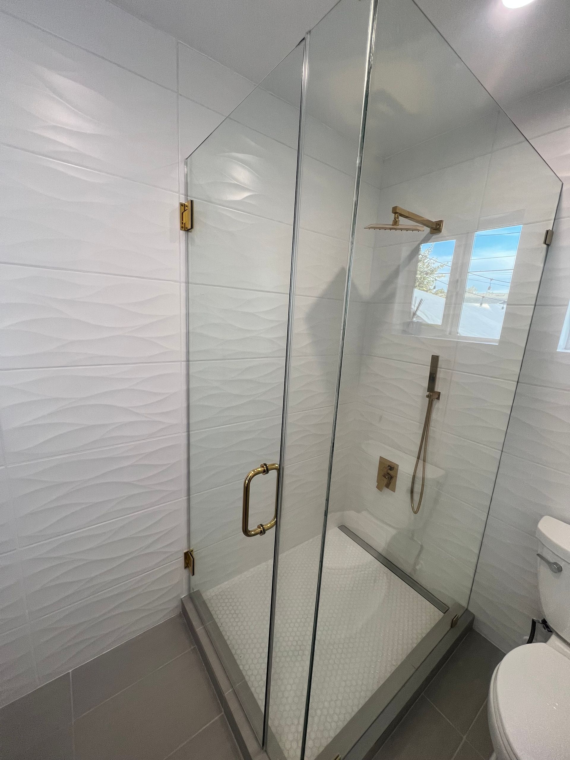 Modern bathroom with a glass shower, toilet, and a bathtub near a window.