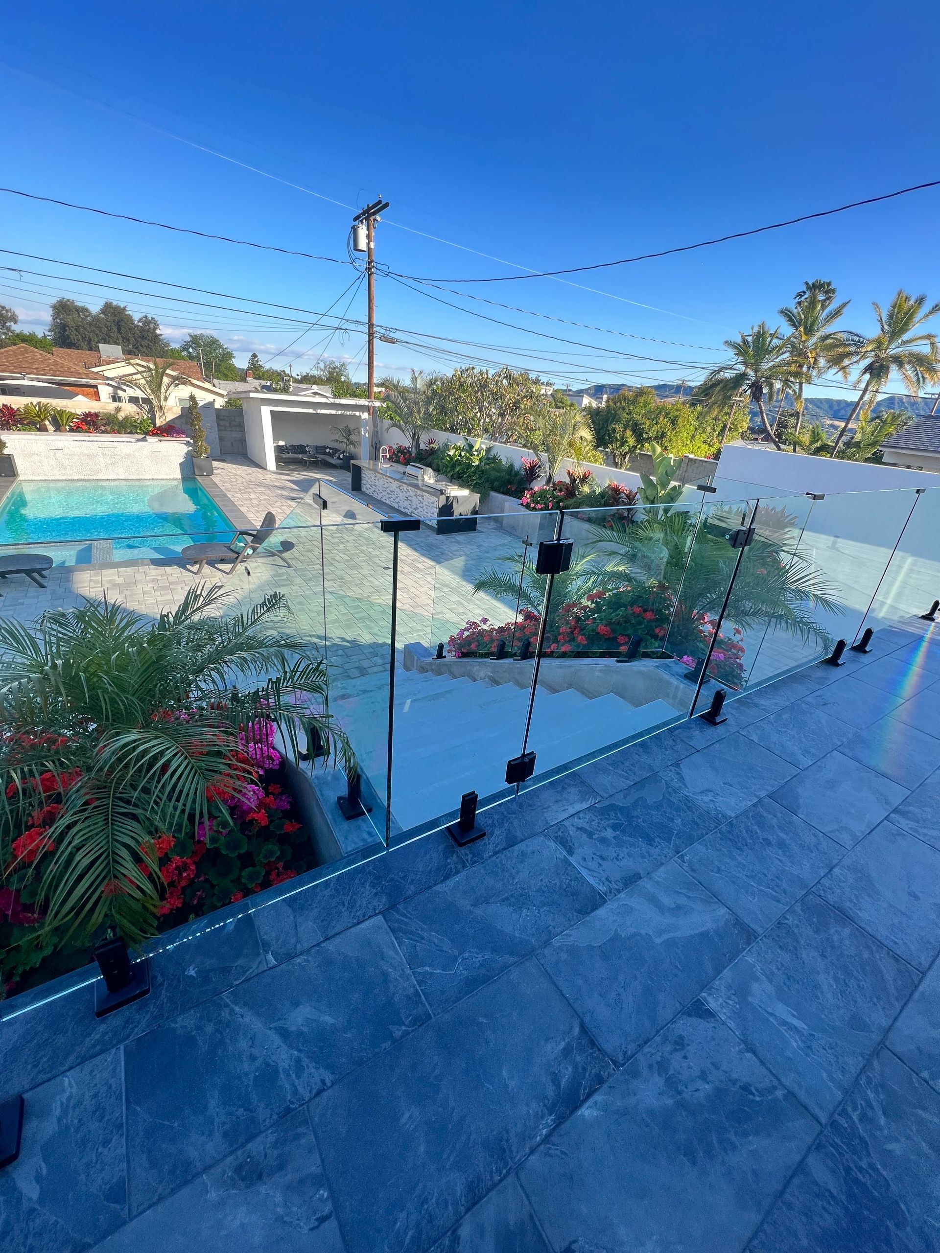 Outdoor patio with a pool, glass railing, landscaping, and blue sky.