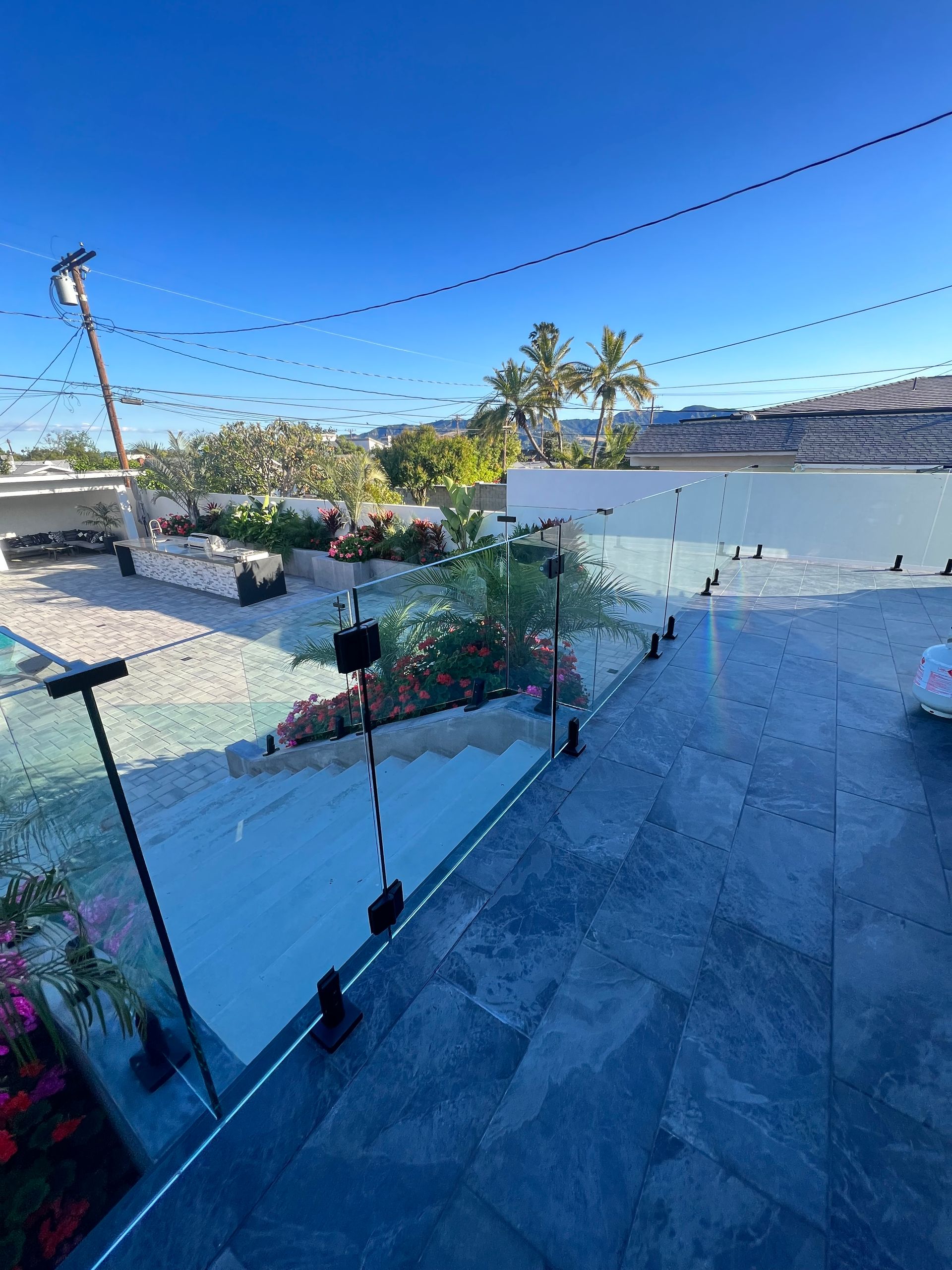 Rooftop patio with glass railing and ocean view under a clear, blue sky.