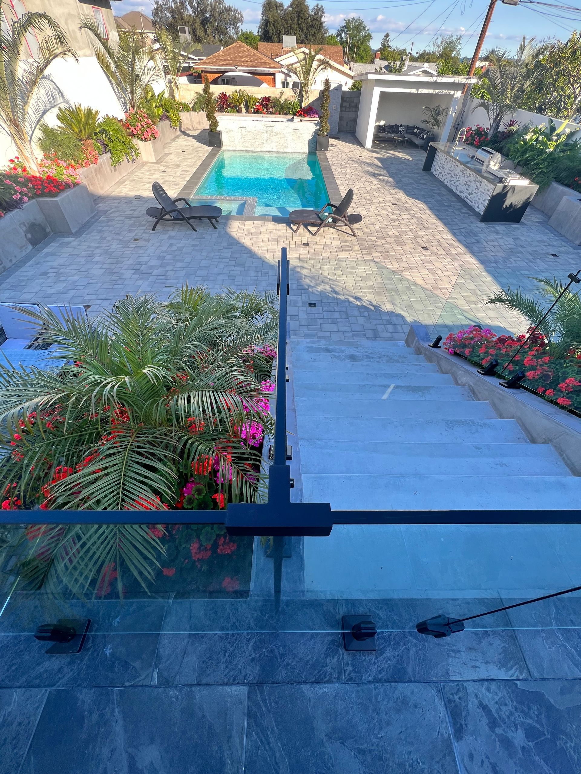 Stairs lead down to a pool and patio area with lush landscaping and lounge chairs.