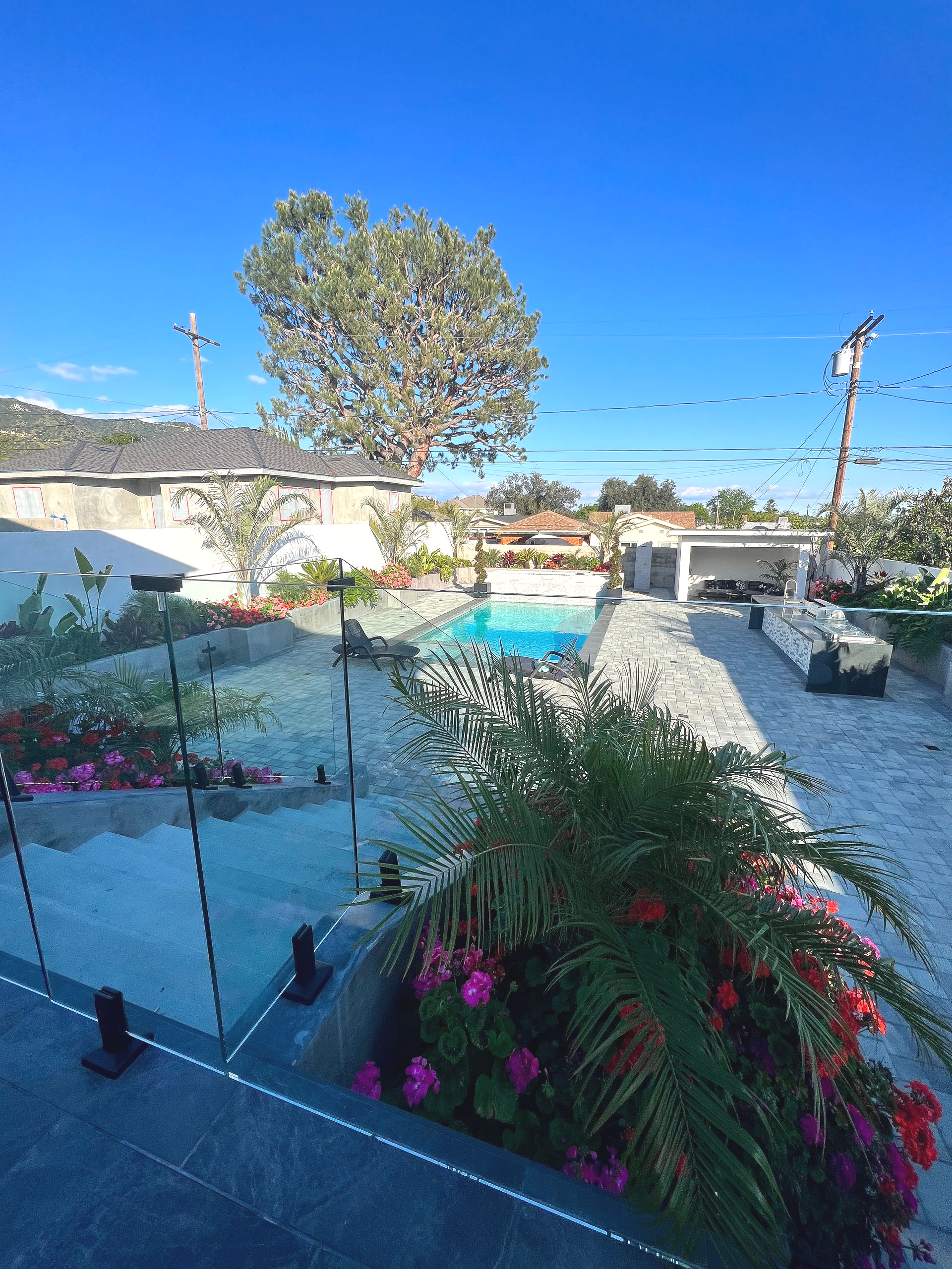 A sunny outdoor scene with a pool, greenery, and buildings under a clear blue sky.