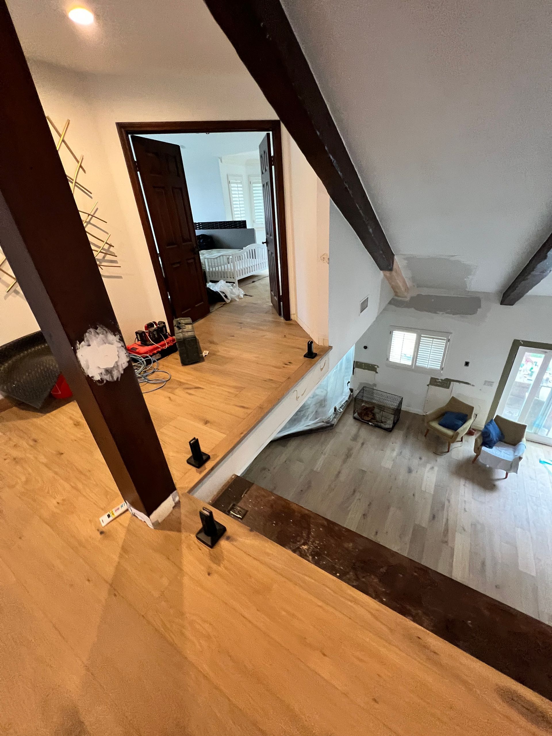 Interior view of a two-story home with exposed wooden beams and light-colored wood flooring.