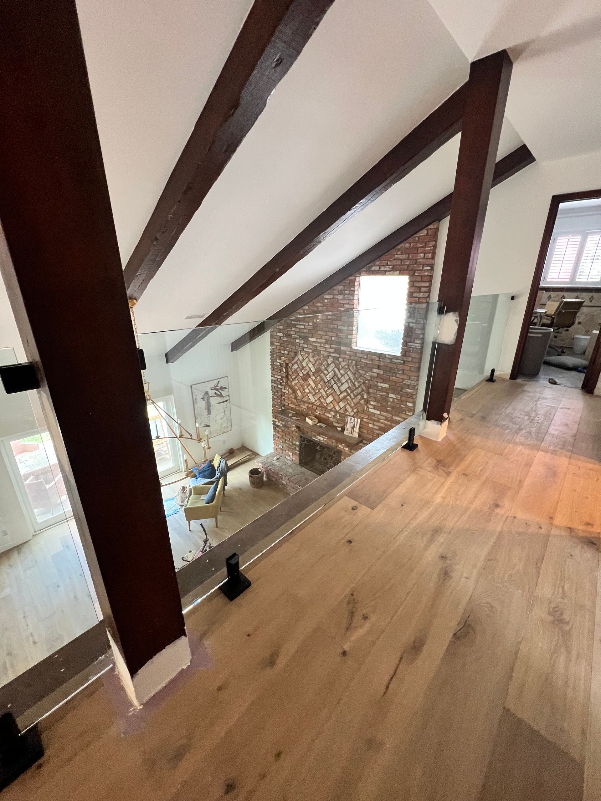 Interior view: wooden beams, glass railing, brick wall, hardwood floor.