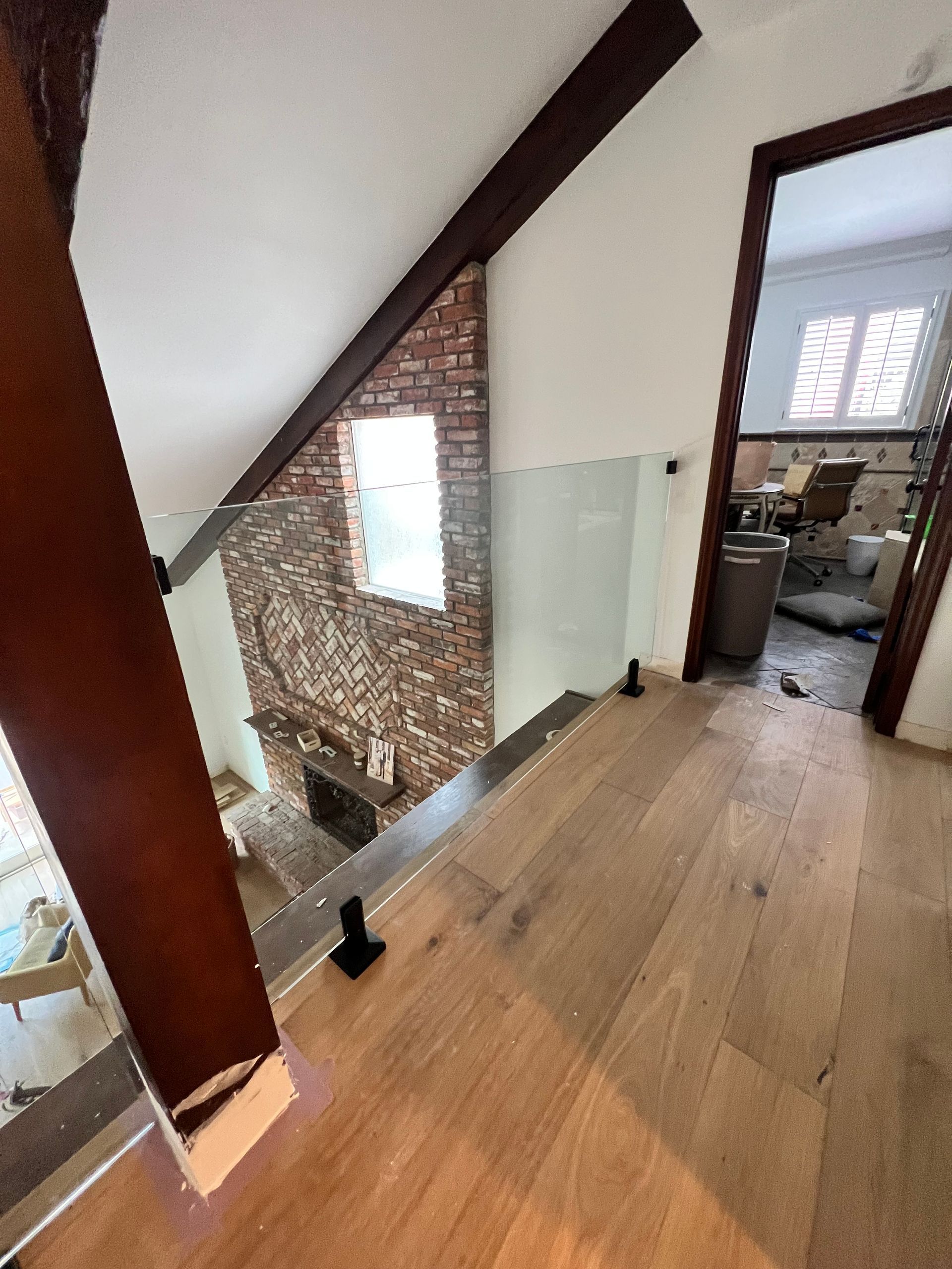 Wooden floor hallway with glass railing and brick wall. Open door to room with a toilet.