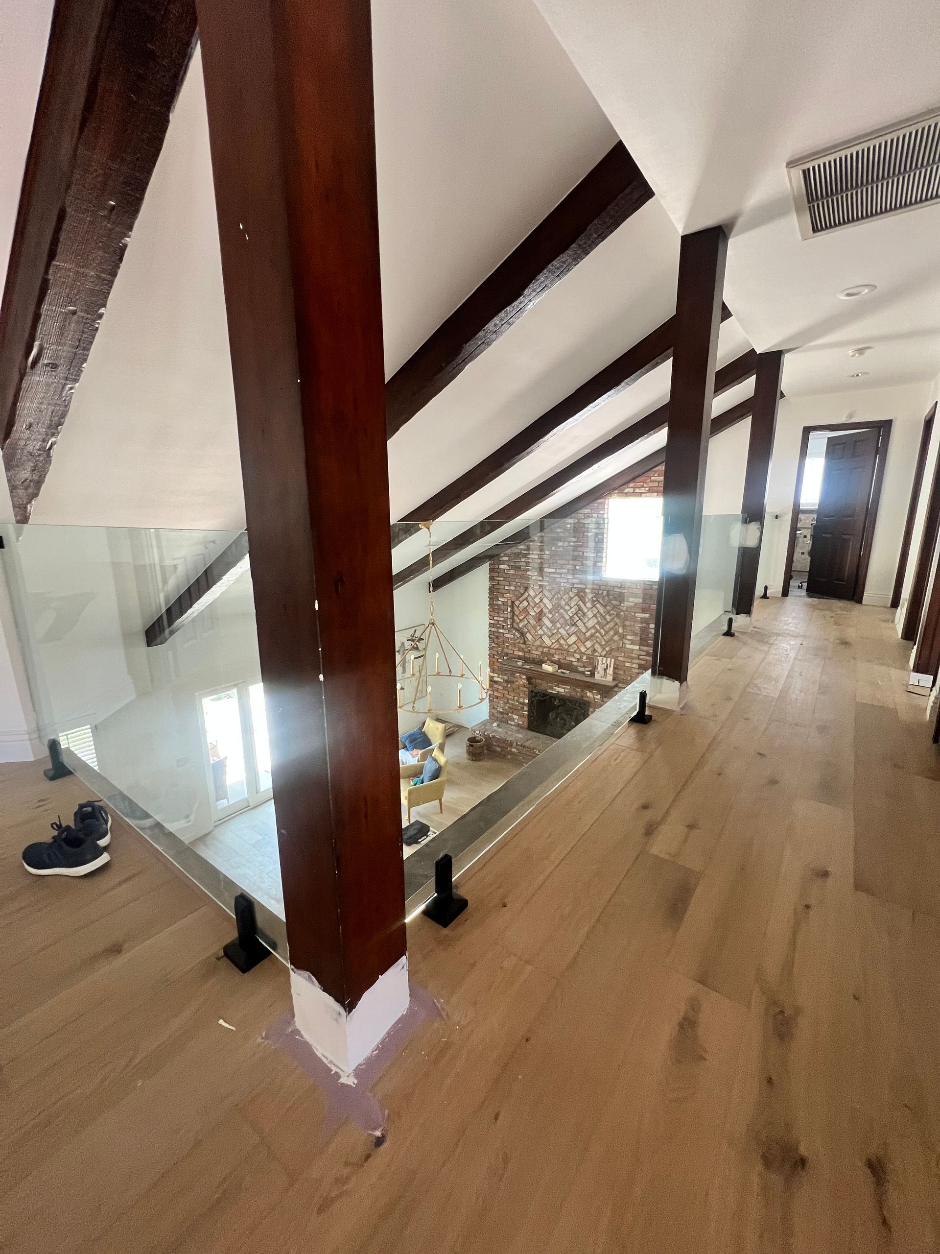 Interior view: glass railing, exposed beams, wooden floor in a hallway.