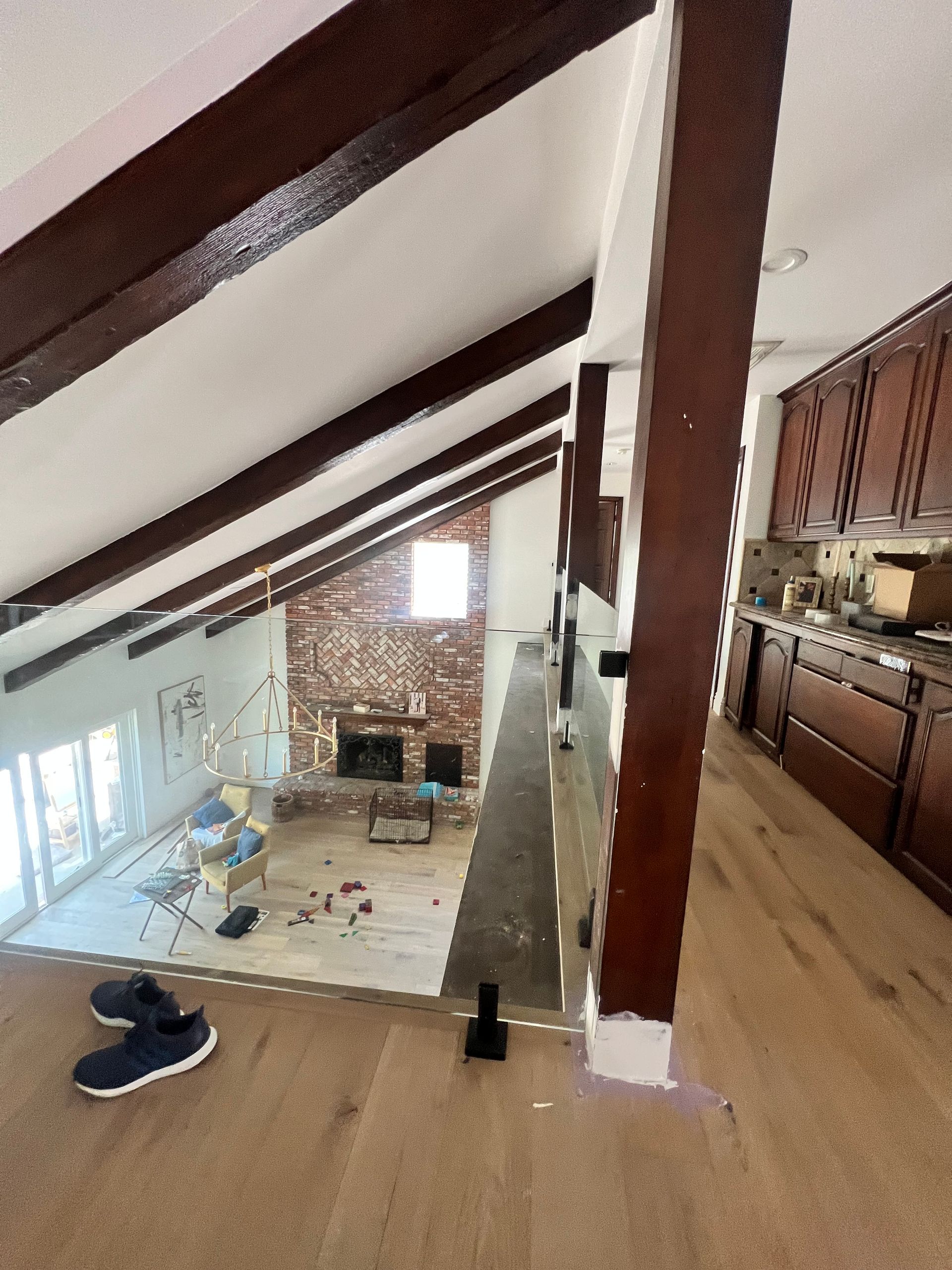 Interior view of a home renovation. Exposed beams, brick fireplace, and kitchen cabinets visible.