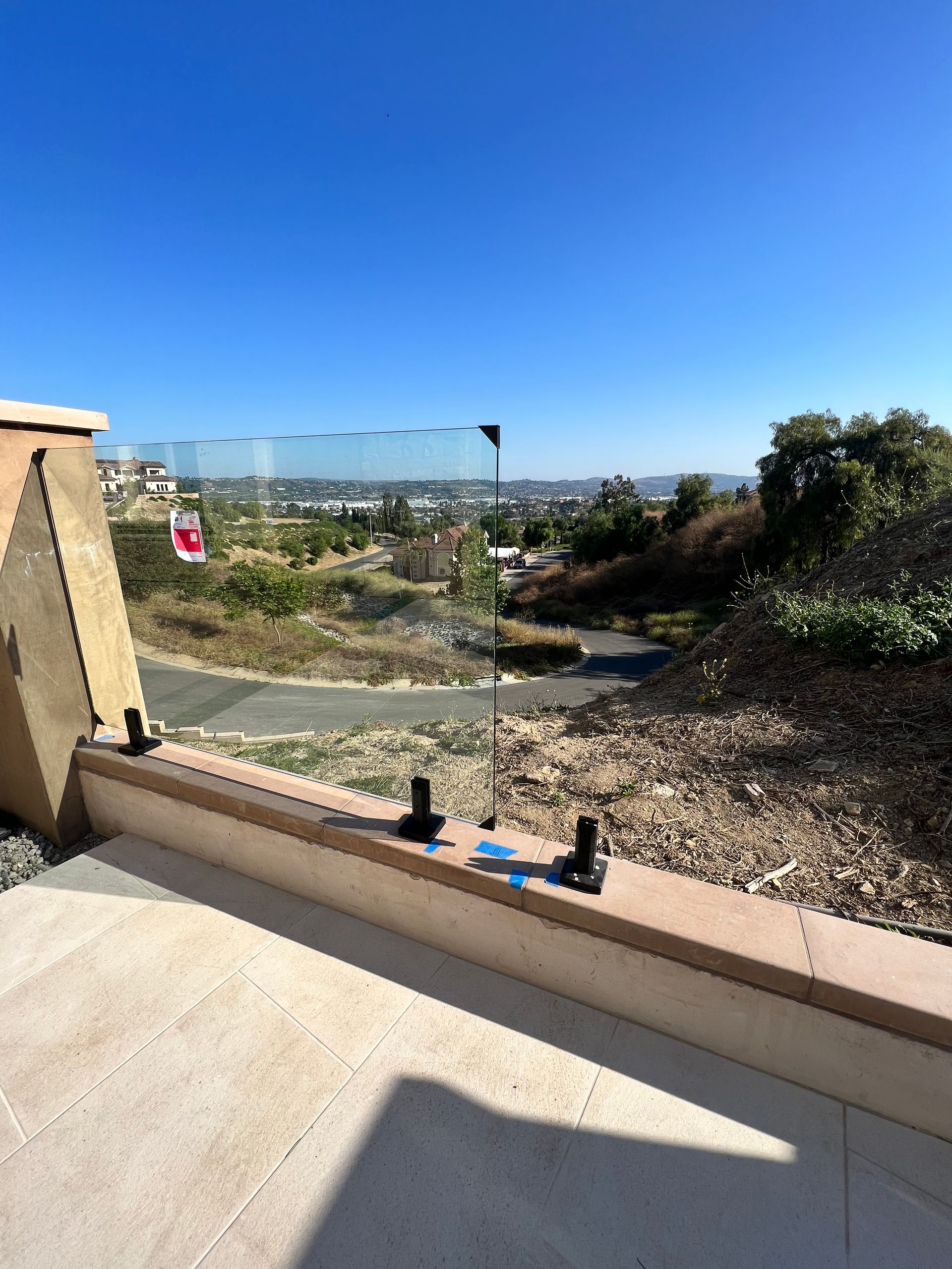 Glass railing on a stone ledge overlooking a landscape under a clear blue sky.