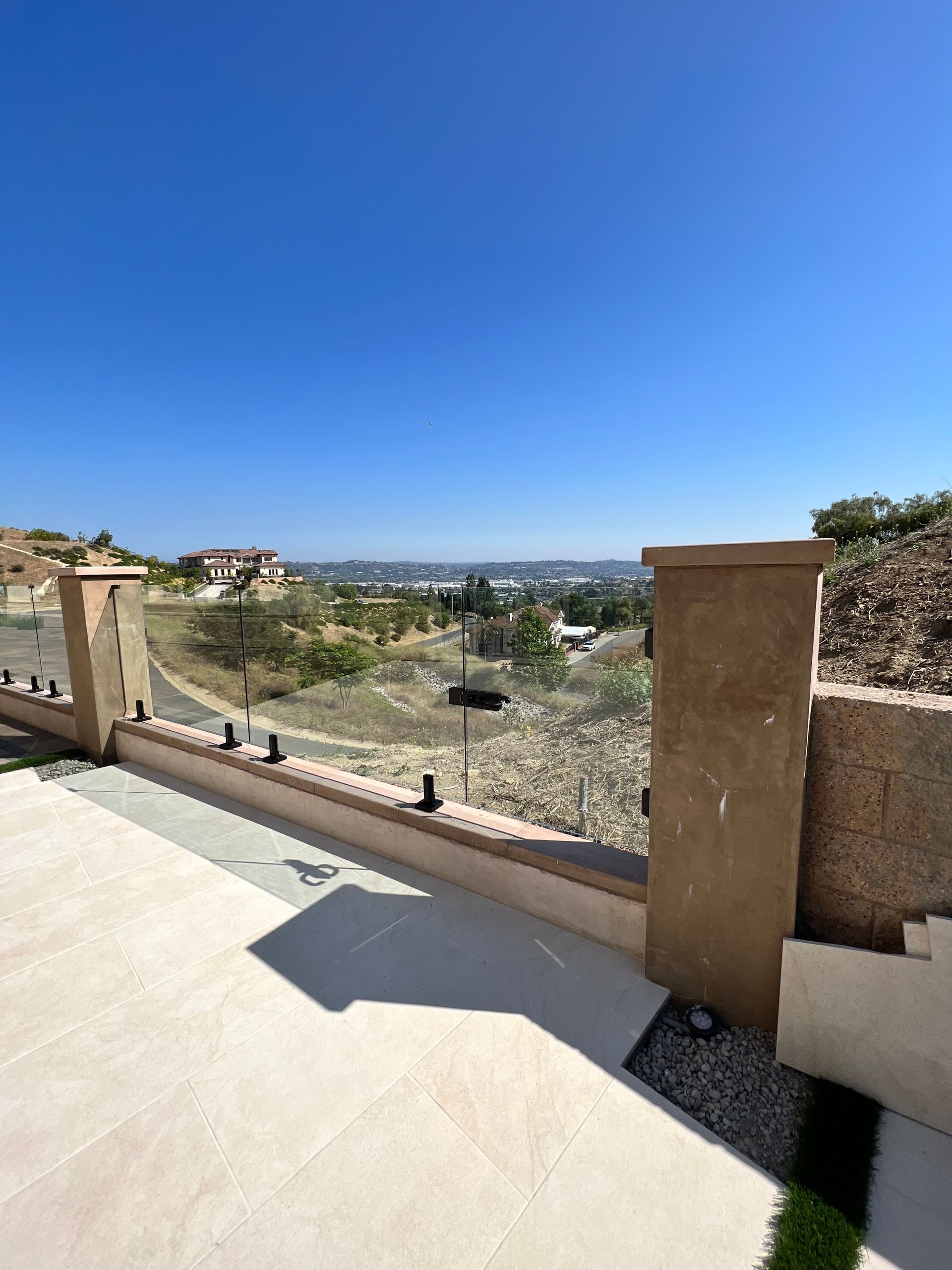 Patio with glass railing overlooking a distant city under a clear blue sky.