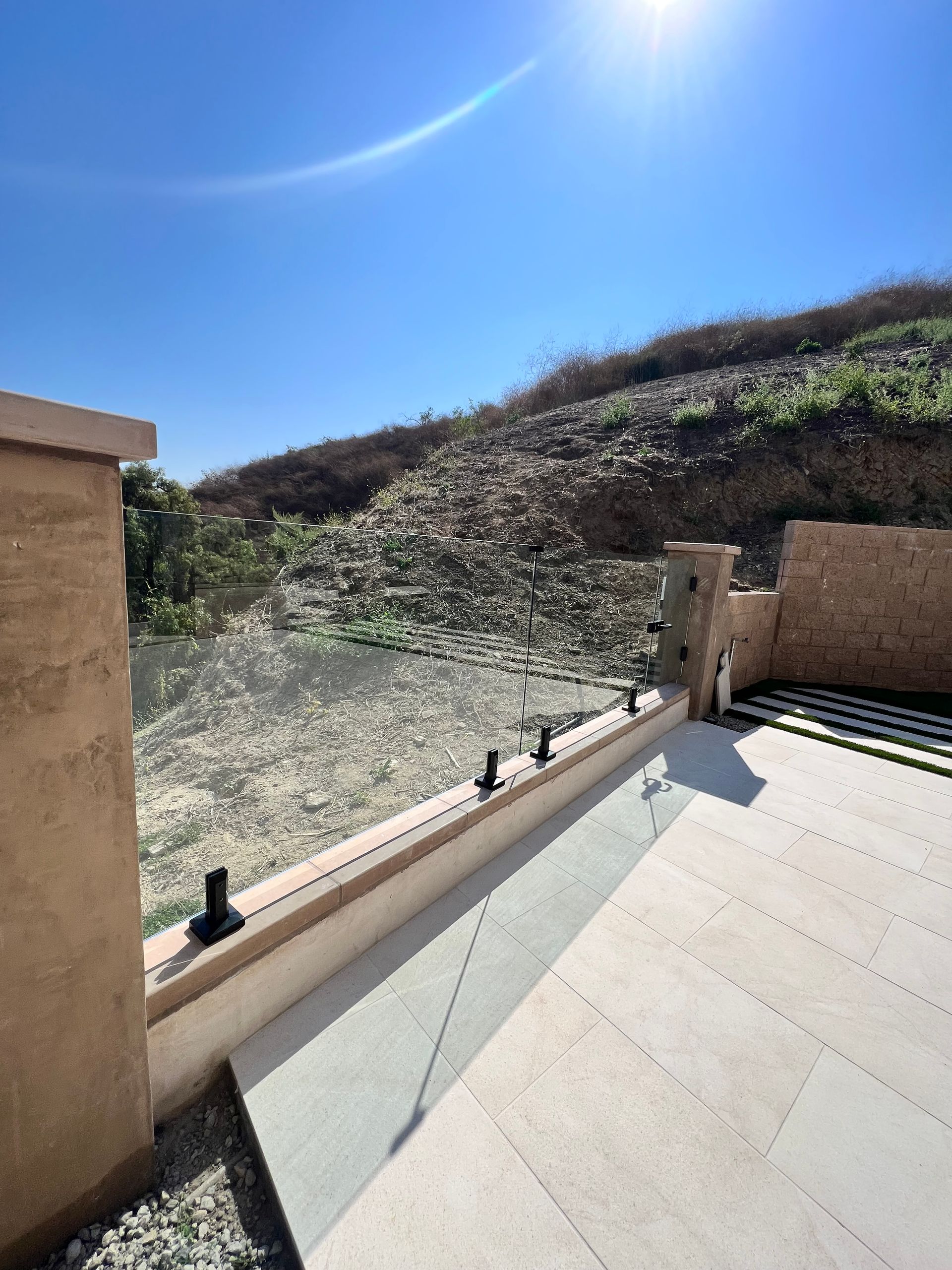 Glass railing on a patio overlooking a hillside under a sunny blue sky.