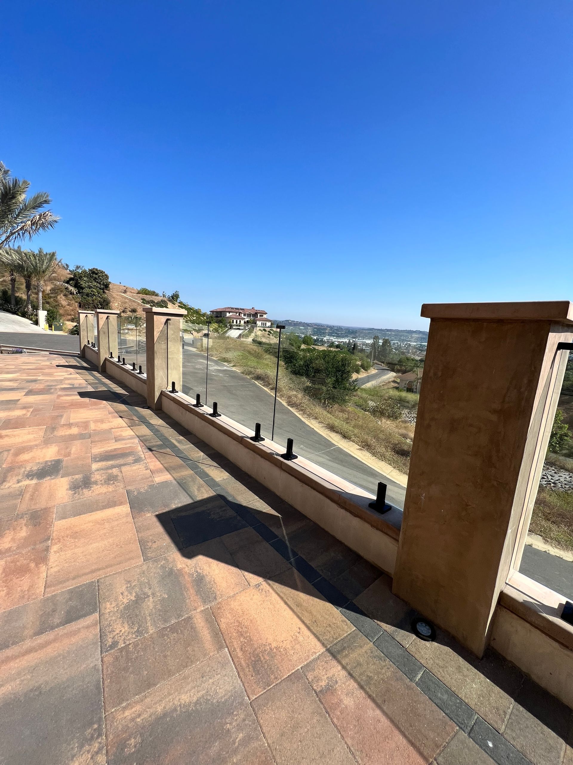Patio with glass railing overlooking a hillside road on a sunny day.