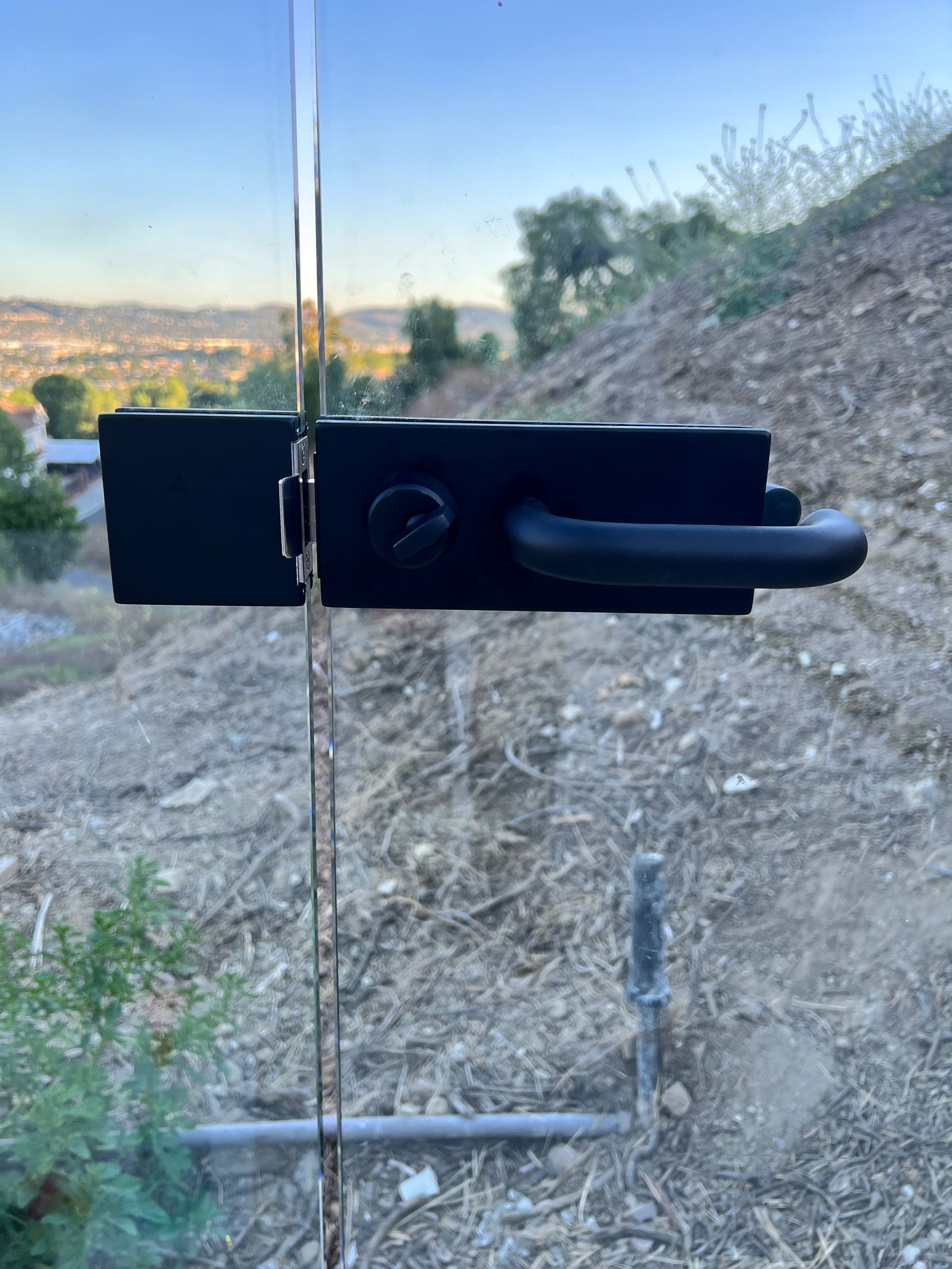 Black door handle and lock on glass door, set against a hillside with a view of a valley.
