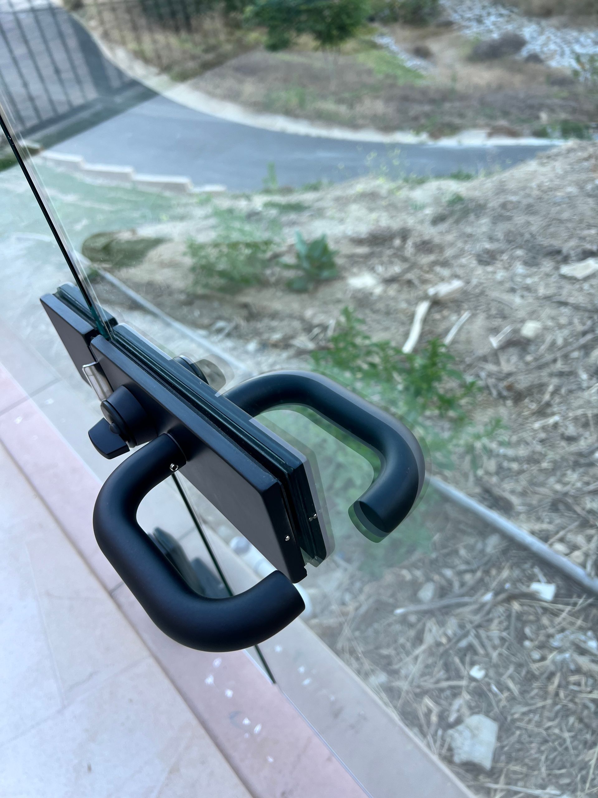 Black tablet attached to glass with suction cups and handle, outdoors.